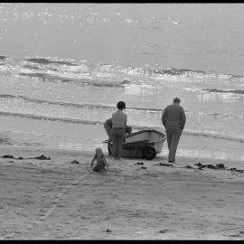 Emptying or loading a dinghy pulled up on Ocean Beach at Mount Maunganui.