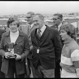 Horse racing. Wife of the owner-trainer of Sakata sharing the Whakatāne Cup with her husband{?} and jockey.