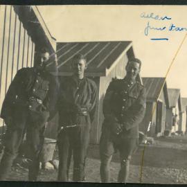 Three men outside huts