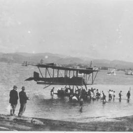 First plane to land in Tauranga is surrounded by children as it floats near the shore. 1920